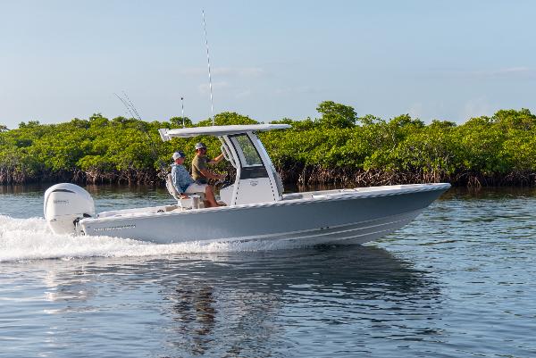 Slide: The Image of 2024 Sportsman Masters 247 Bay Boat cruising on water near lush greenery. - 0