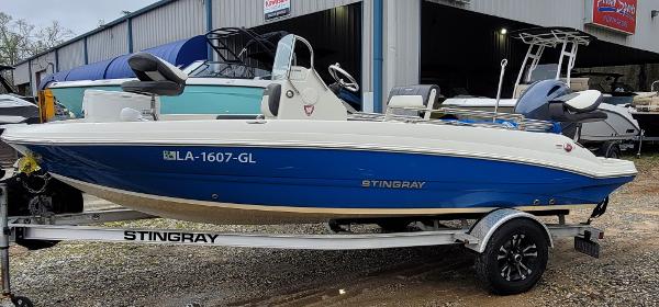 Slide: The Image of 2019 Stingray 186 CC boat on trailer, blue and white, parked outside a building. - 2