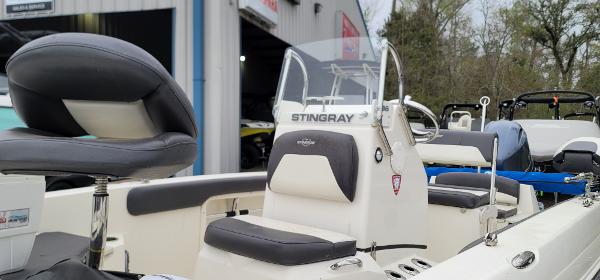 Slide: The Image of 2019 Stingray 186 CC boat interior with seating and console, parked near a building. - 7