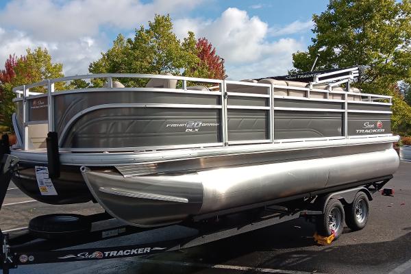 Slide: The Image of 2024 Sun Tracker Fishin' Barge 20 DLX pontoon boat on trailer, parked outdoors. - 0