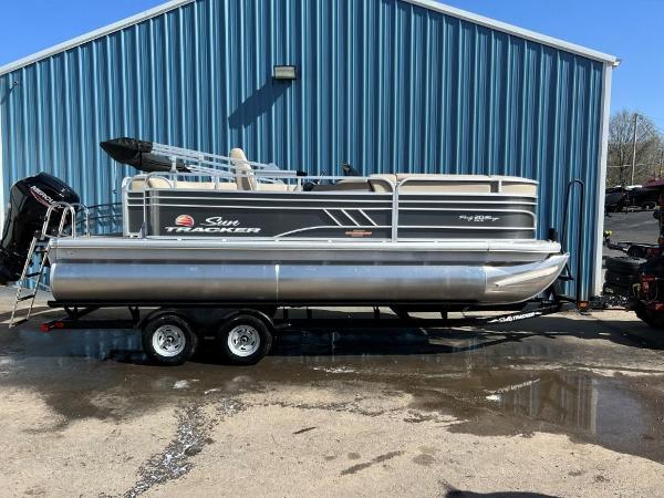 Slide: The Image of 2023 Sun Tracker PARTY BARGE® 20 DLX pontoon boat on a trailer outside a blue building. - 0