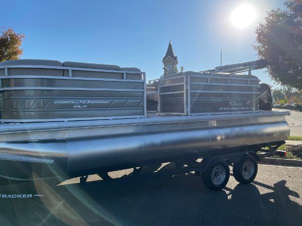 Slide: The Image of 2024 Sun Tracker Party Barge 20 DLX pontoon boat on trailer in sunny outdoor setting. - 1