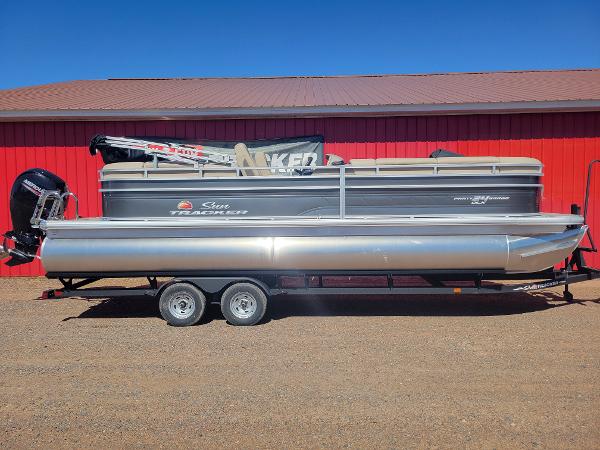 Slide: The Image of 2024 Sun Tracker Party Barge 24 DLX pontoon boat on trailer, red building background. - 0