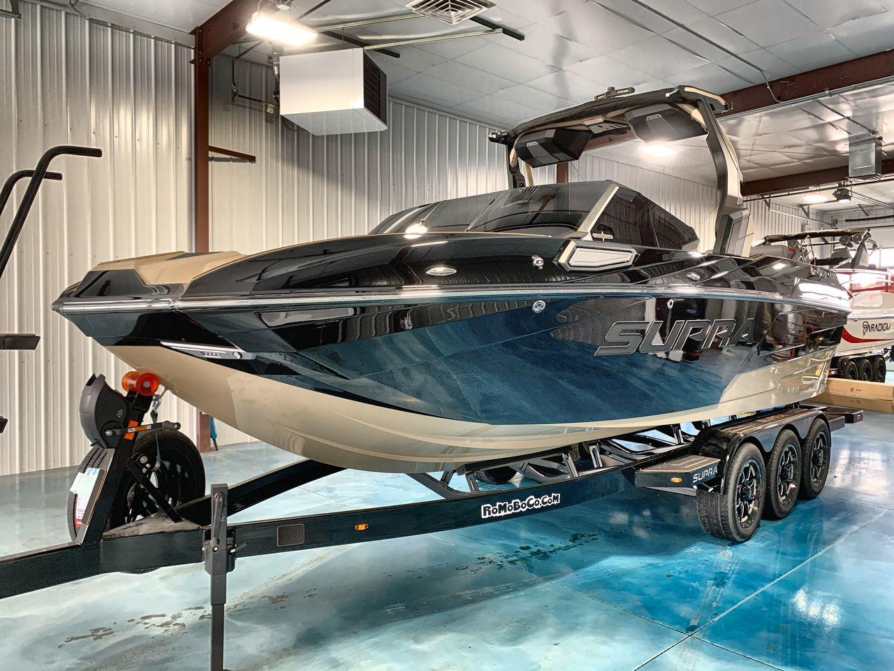 Slide: The Image of 2025 Supra SE boat in showroom, sleek design, black and beige color, on trailer. - 1