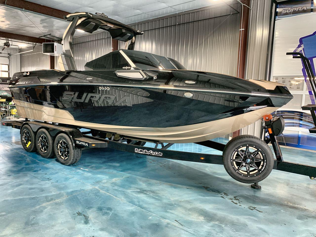 Slide: The Image of 2025 Supra SE boat on trailer in showroom, sleek black and beige design. - 5