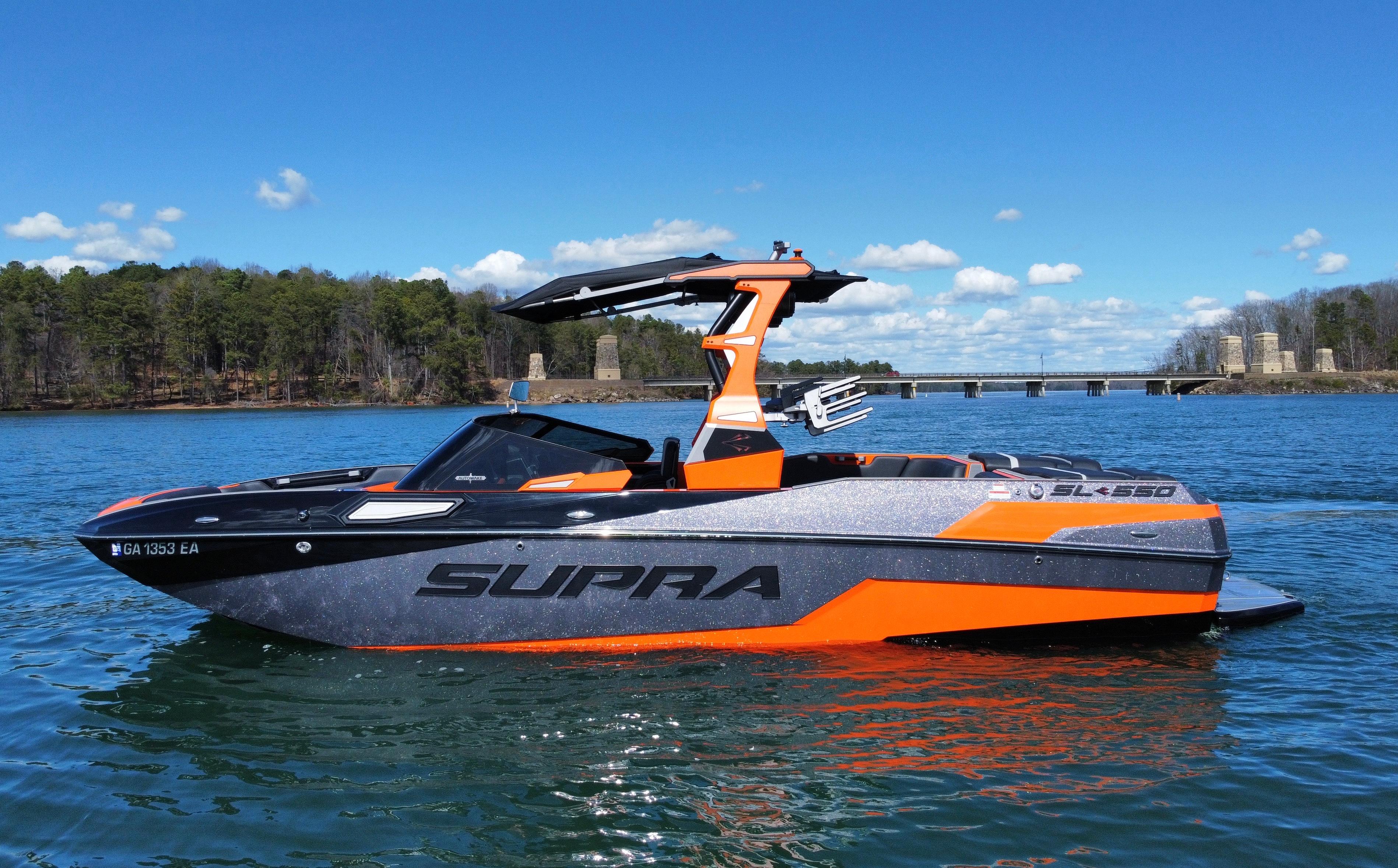 Slide: The Image of 2022 Supra SL 550 boat on a lake with a bridge and trees in the background. - 1