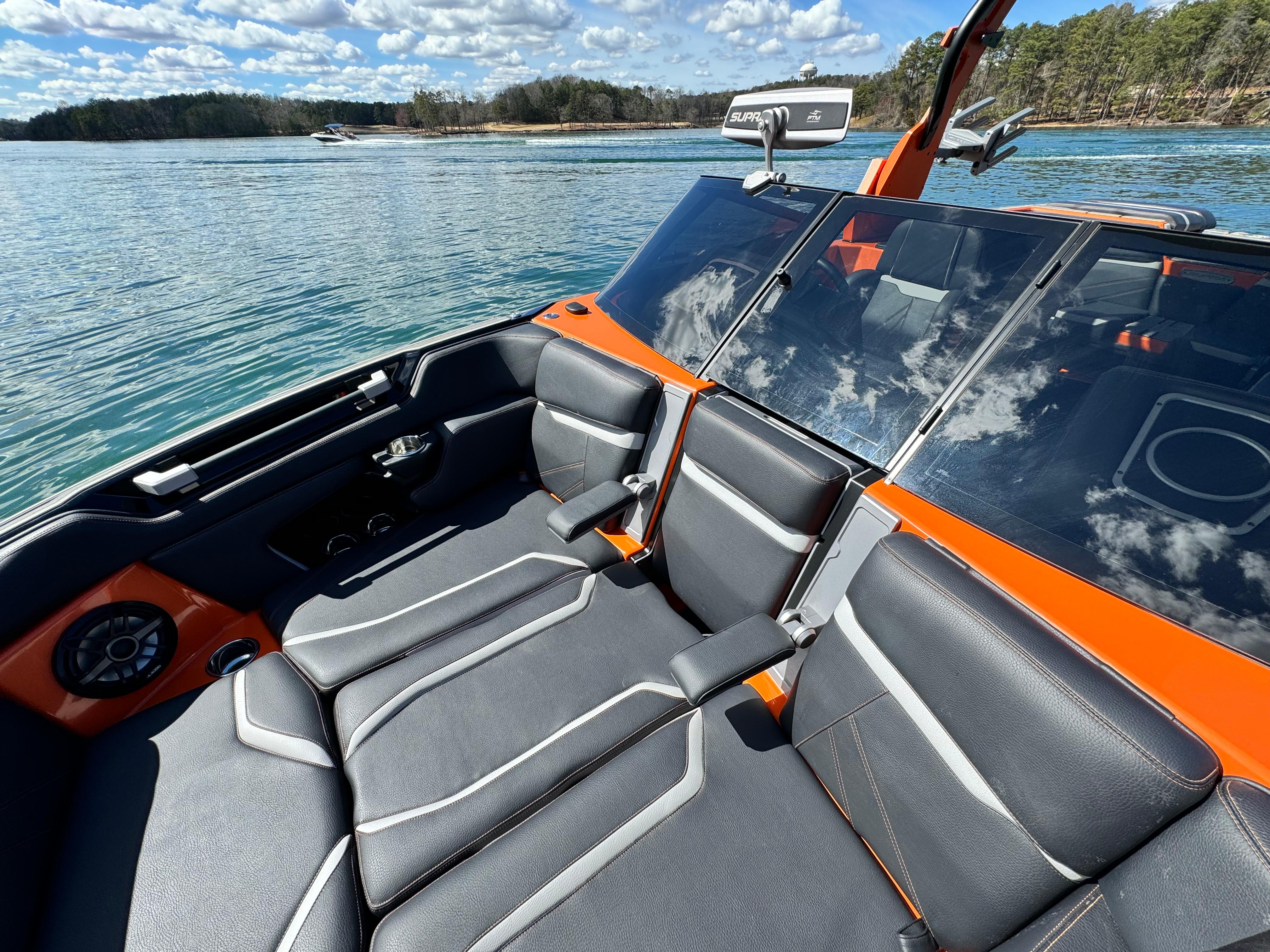 Slide: The Image of 2022 Supra SL 550 boat interior with sleek black and orange seating on a sunny lake. - 2