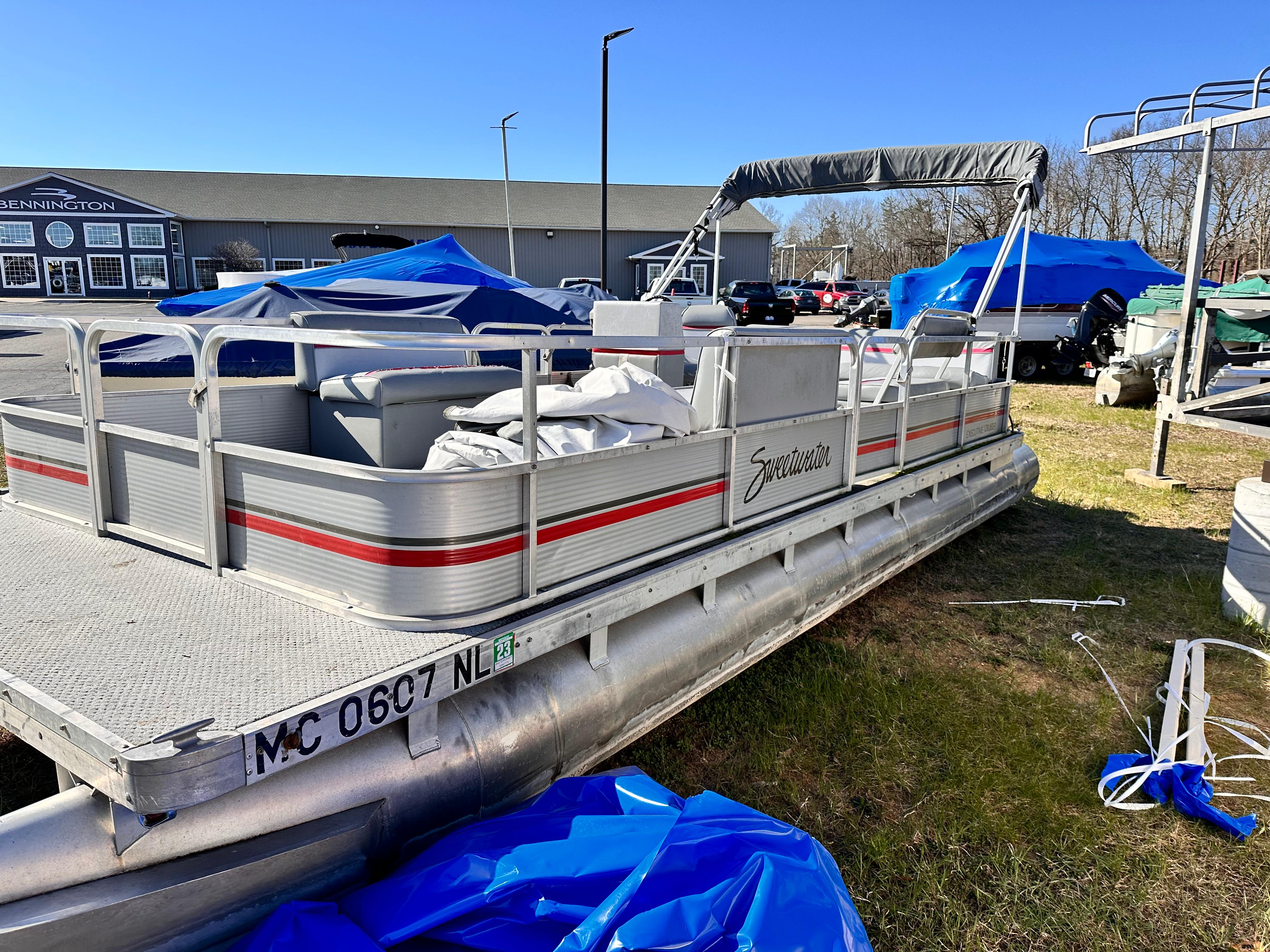 Slide: The Image of 1987 Sweetwater Pontoon boat in a storage yard with blue tarps and other boats. - 2