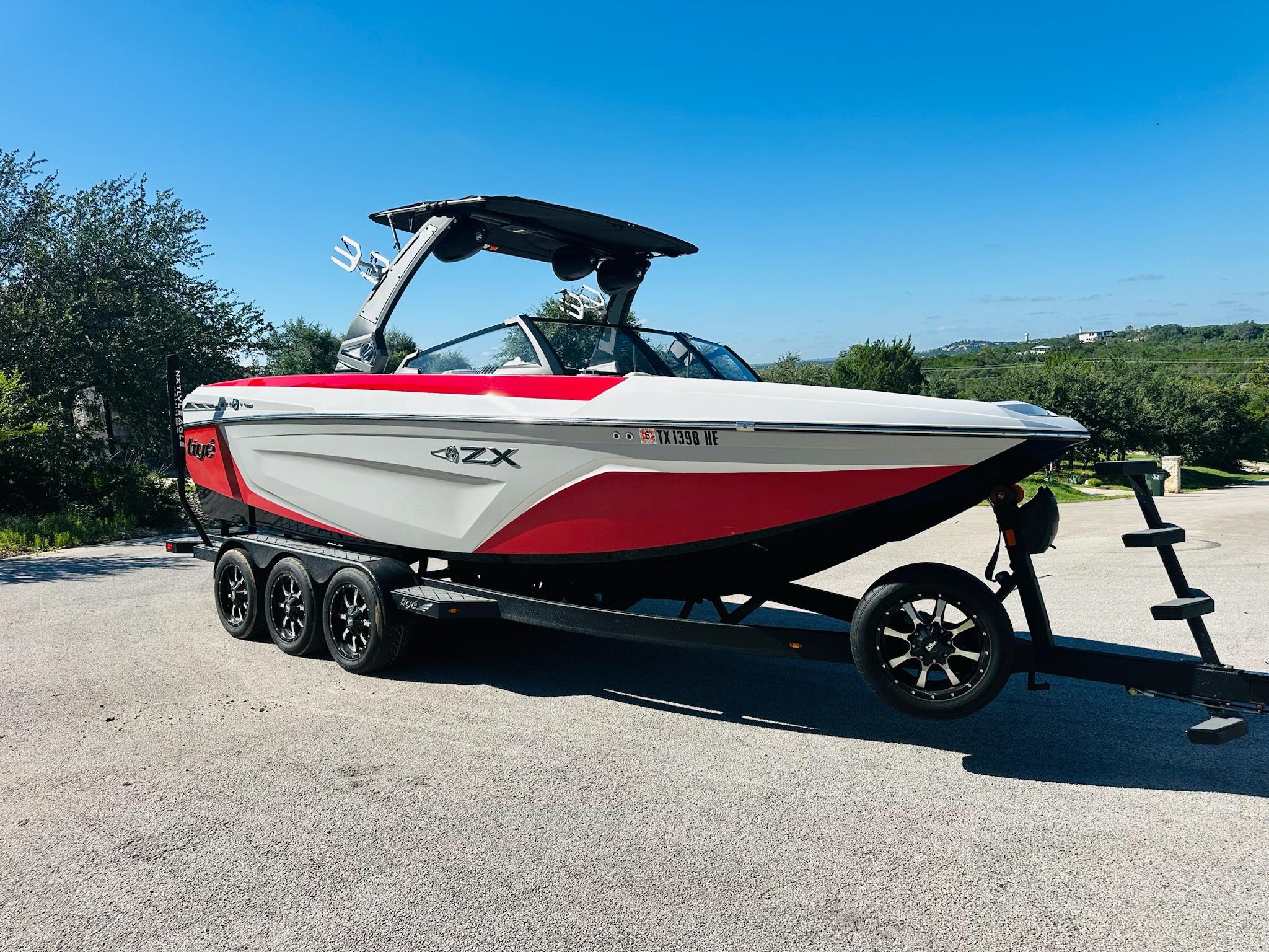 Slide: The Image of 2020 Tigé 25ZX boat on trailer, red and white design, parked outdoors under clear blue sky. - 8