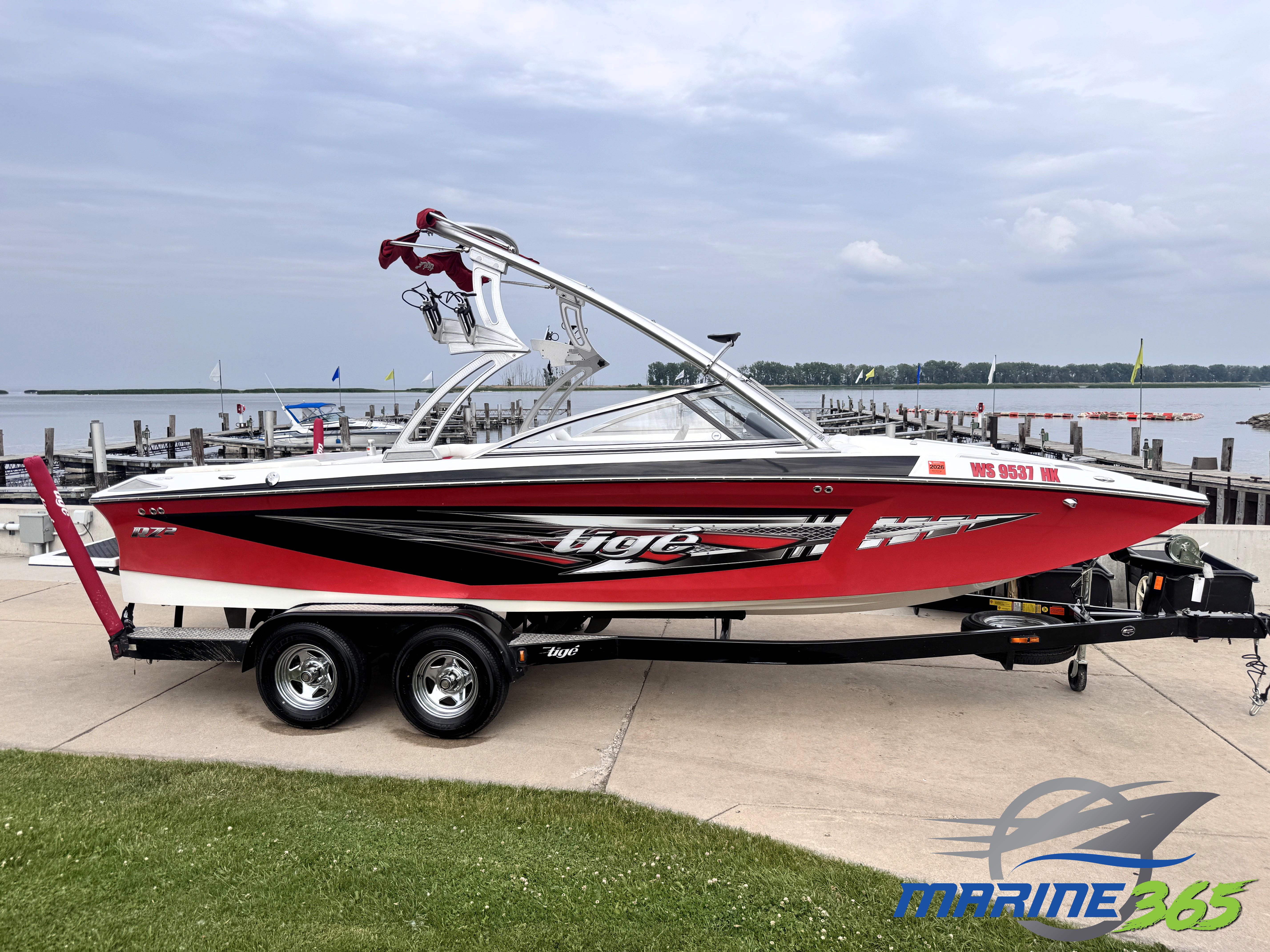 Slide: The Image of 2007 Tigé RZ2 boat on trailer by marina, red and black design. - 0