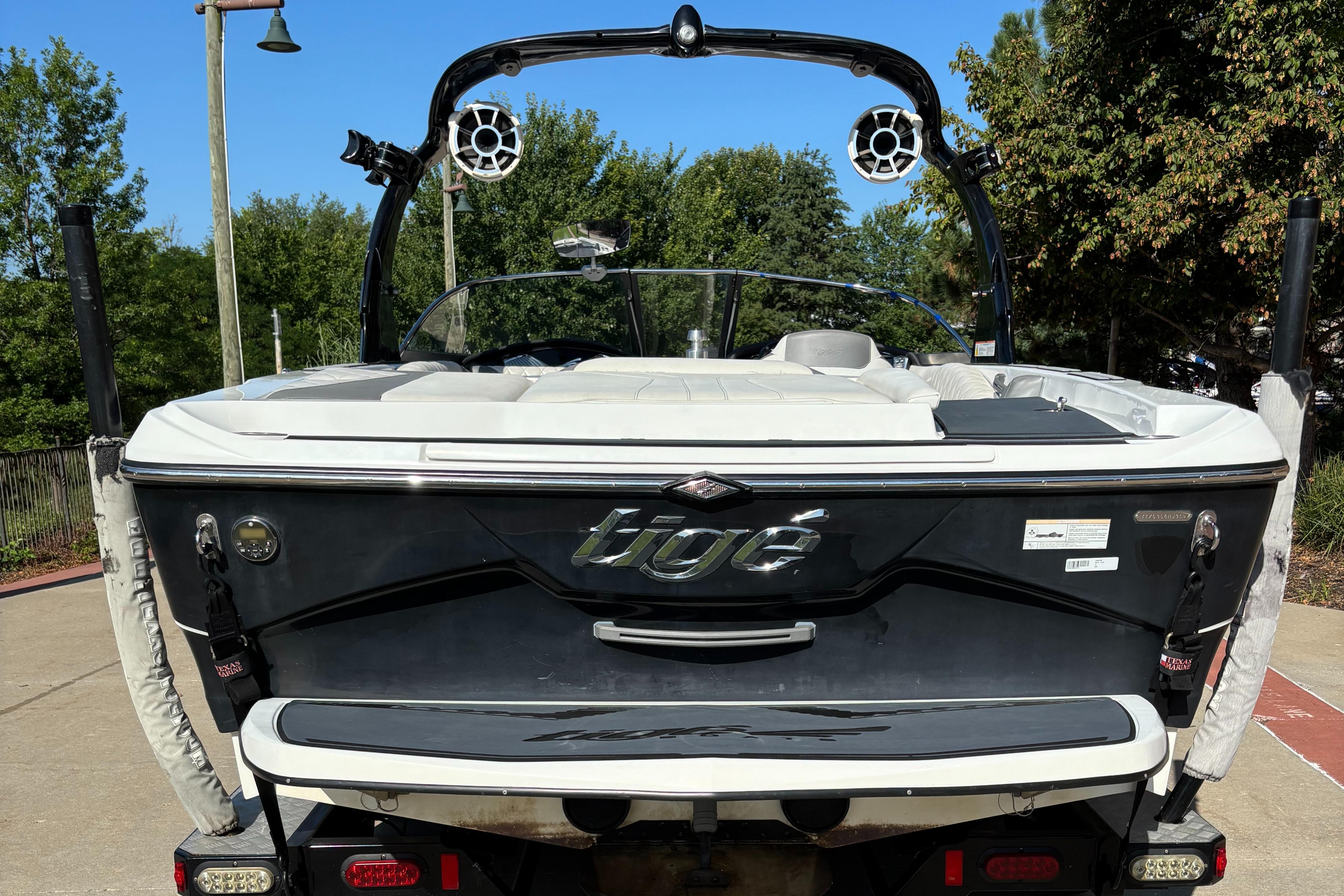 Slide: The Image of 2014 Tigé RZR boat, rear view, parked outdoors with trees in the background. - 1