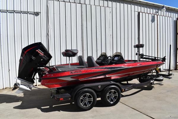 Slide: The Image of 2024 Triton 18 TrX bass boat in red and black, parked on a trailer. - 2