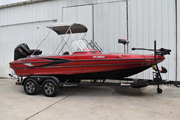 Slide: The Image of 2024 Triton 206 Allure red fishing boat on trailer, parked near a metal building. - 2