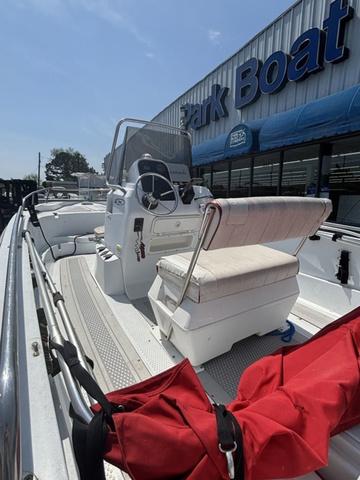 Slide: The Image of 2002 Triumph 190 Bay boat with seating, steering console, and red bag, parked outside a boat dealership. - 2