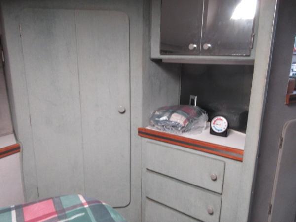 Slide: The Image of 1986 Trojan 11 Meter Convertible cabin interior with storage cabinets and plaid bedding. - 20