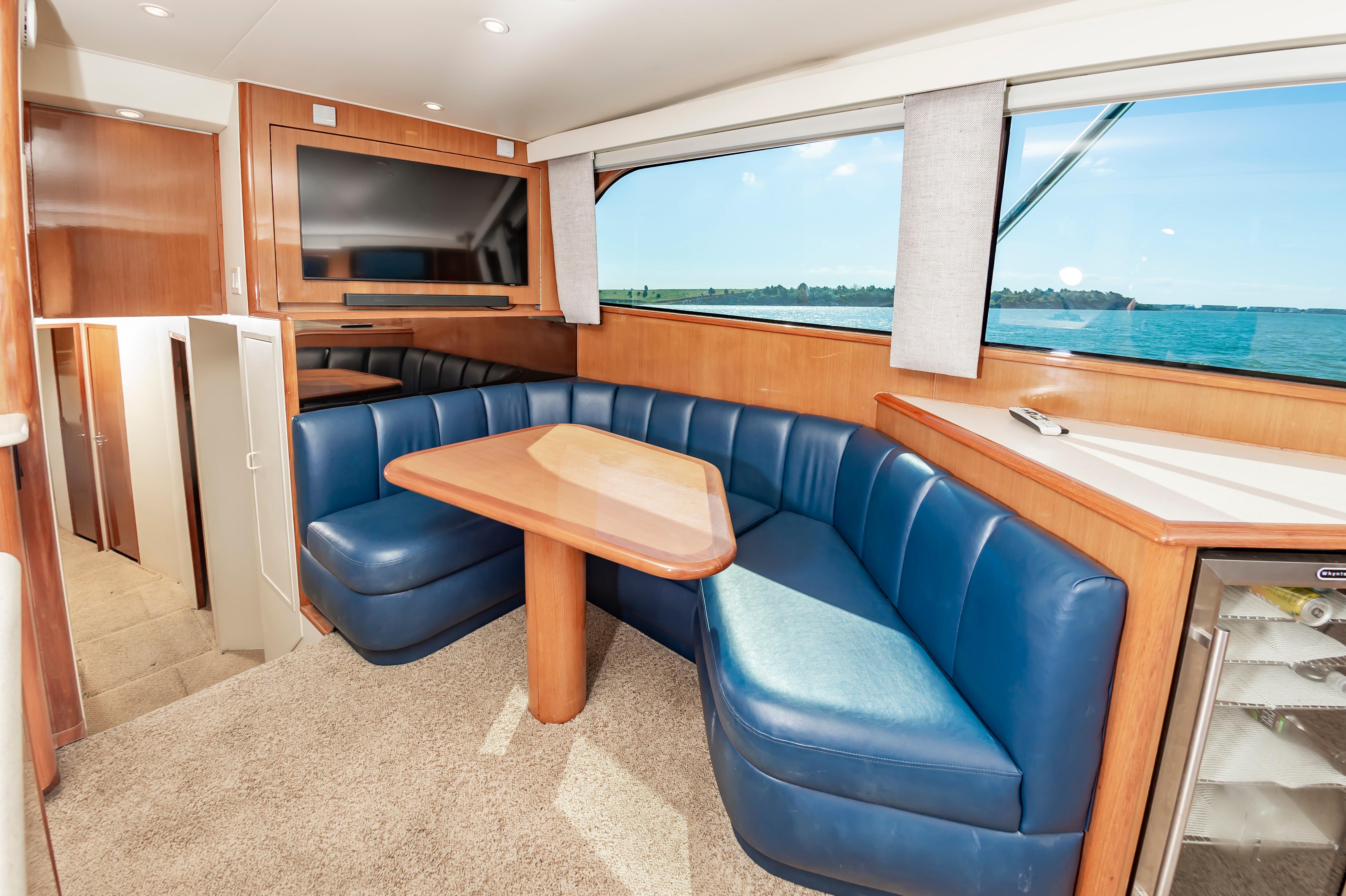 Slide: The Image of 1998 Viking Convertible yacht interior with blue leather seating, wooden table, and large window. - 35