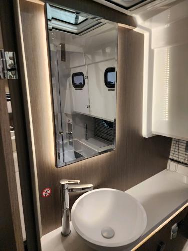 Slide: The Image of 2024 Wellcraft 355 Commuter bathroom with modern sink, mirror, and porthole windows. - 6