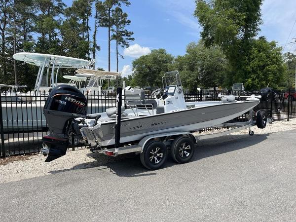 Slide: The Image of 2025 Xpress H22B boat on trailer, parked outdoors near trees and other boats. - 2