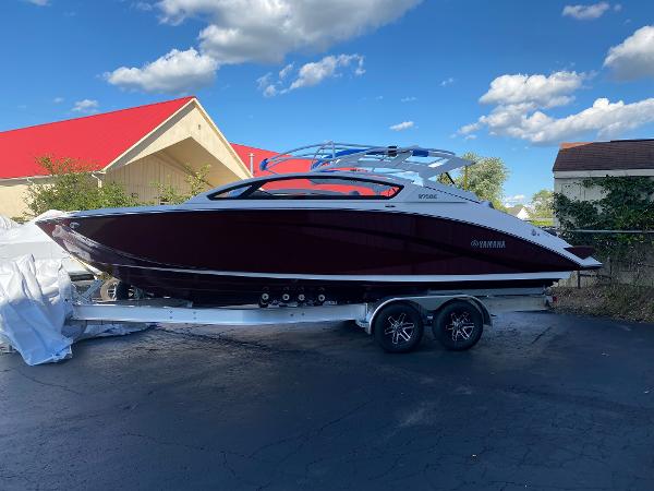 Slide: The Image of 2023 Yamaha Boats 275SE on trailer, sleek design, red and white exterior, under blue sky. - 2